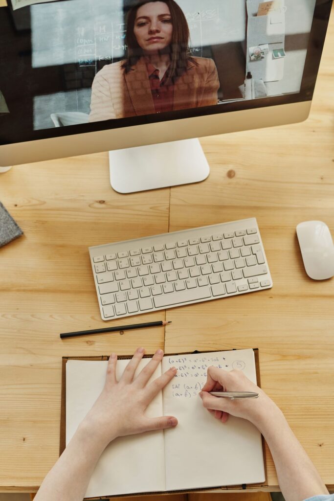 Étudiante prenant des notes pendant une session de formation en ligne avec un enseignant visible sur l'écran